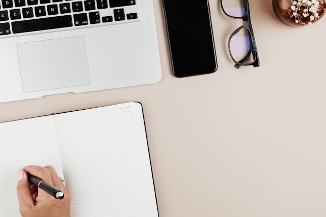 Ecriture sur un carnet de notes près d’un ordinateur portable, espace de travail d’écriture organisé